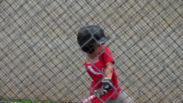 A boy practices baseball at a batting cage with a red white and blue American flag bat. alt