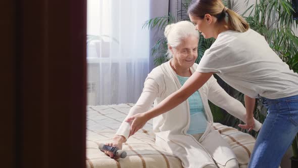 Elderly Woman Exercising with Dumbbells with Help of Caregiver 