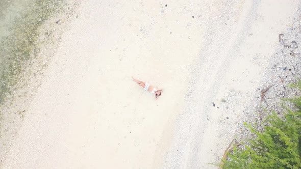 Smiling Woman Lying on White Sand at Sea Beach Aerial View. Top View Young Brunette Woman Relaxing alt