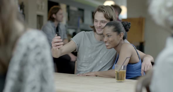 Man holding mobile phone and talking with woman while drinking beer in pub