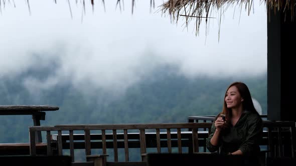 A young female traveler drinking coffee with a beautiful foggy mountain and nature view.