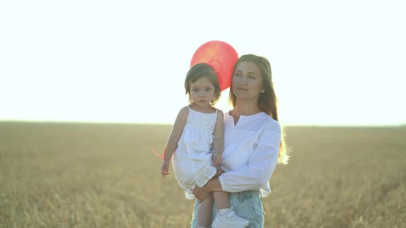 Mother with Daughter and Balloons Walking on Wheat Field