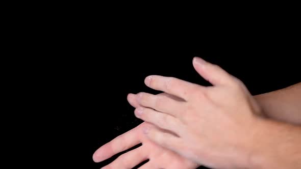 A person rubbing and dusting his hands with chalk powder, isolated on black background. Slow motion. alt