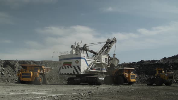 Group of Technological Transport Around Huge Mining Excavator