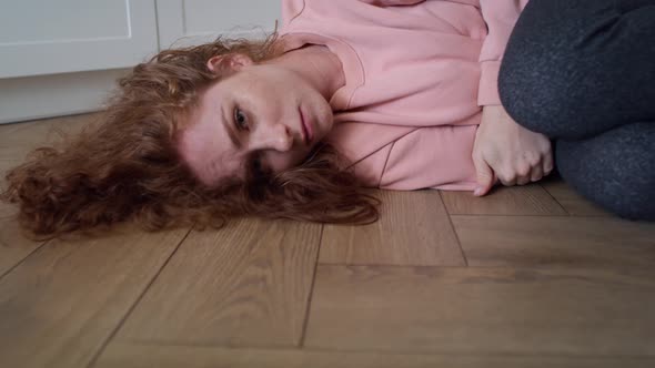 Zoom in video of depressed young caucasian woman lying in the floor. alt