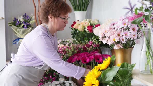 Serious female entrepreneur preparing flowers for new busy working day in floristic street shop.