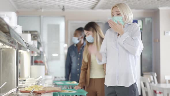 Ill Young Blond Woman in Face Mask Sneezing and Queue Moving Away in Lunchroom alt