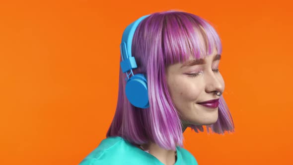Attractive Modern Woman Dancing with Headphones on Orange Studio Background alt