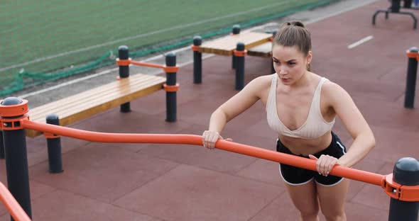 Beautiful Athletic Young Woman in Sportswear Doing Pushups Using the Bar on the Sports Ground