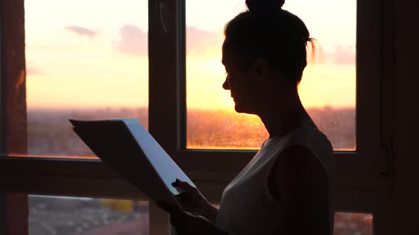 Businesswoman Using Tablet and Looks at Work Papers with Sunbeams and Lens Flare Effects Against