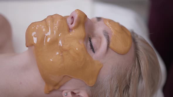 Closeup Face of Beautiful Woman with Closed Eyes and Yellow Honey Mask on Facial Skin alt