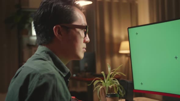 Asian Male Works With Mock Up Green Screen Computer Display. He Works At Night alt