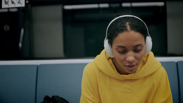 Young Girl Looks at Her Phone Listens Music in Headphones Sitting in Metro alt