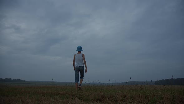 Boy Walks on a Field in Rainy Weather in the Evening