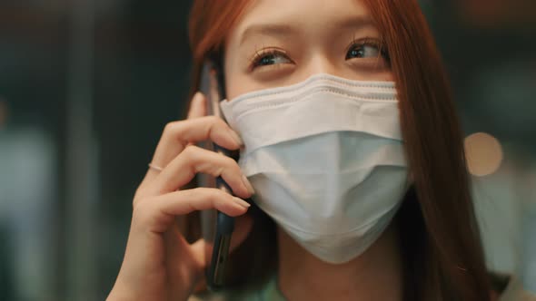 Young Beautiful Asian woman wearing a medical protective face mask talking on a smartphone