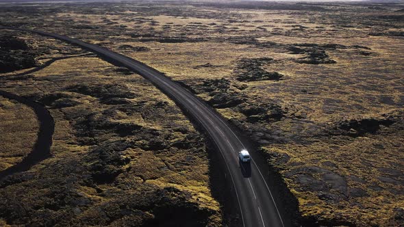 Car on remote empty road surrounded by Iceland tundra landscape, bright sunshine on horizon, aerial alt