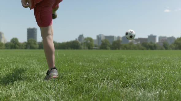 Static slomo shot of toddler kicking soccer ball in field on bright sunny day. Low POV alt