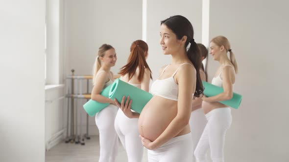 Expectant Woman Posing at Camera in Yoga Studio While Group of Females Stand in the Background