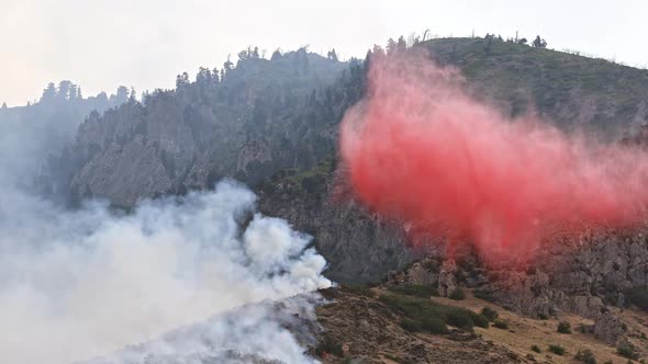 Small airplane dropping fire retardant on wildfire burning on mountainside alt