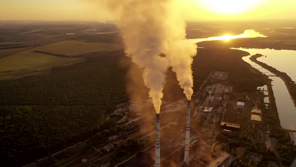 Manufacturing in nature at sunset. White smoke goes from metallurgical pipes into the air.  alt