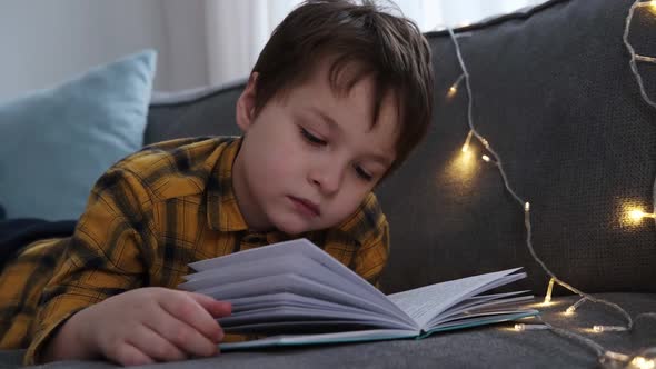 Little Boy Lies on the Couch and Reads a Book