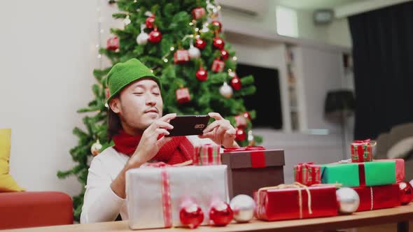 Attractive Asian men taking a photo gift box on a smartphone decorate Christmas tree.