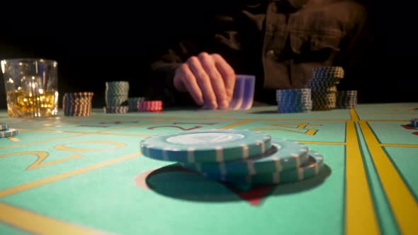 Unrecognizable Male Player Sits at Gaming Table in Casino and Drinks Whiskey From Glass alt
