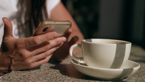Closeup of a White Cup with a Saucer and a Female Hands with a Phone alt