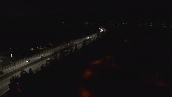 Cars driving at night on illuminated highway. Track left drone shot. alt