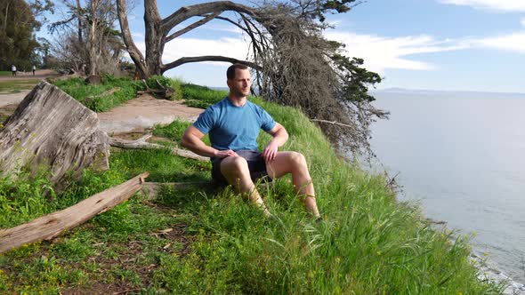 A man sitting down into a meditation pose to practice mindfulness and relieve stress after a workout alt