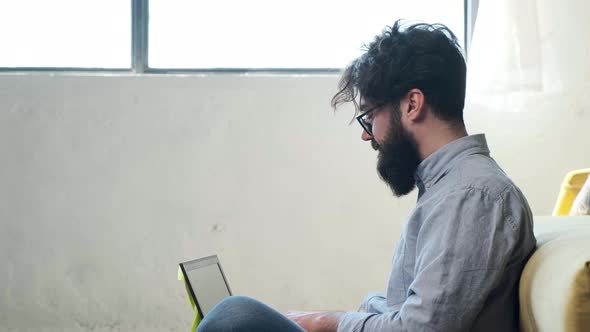 Man Working at the Computer with a Lot of Reminder Notes Sitting Near Sofa alt