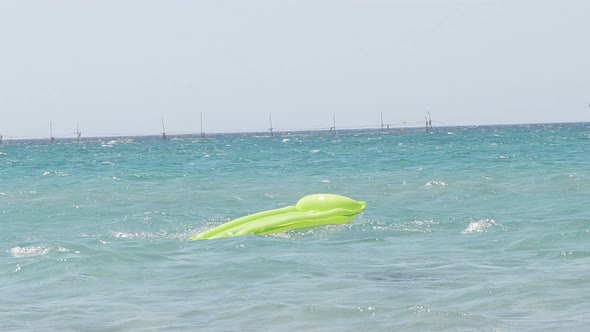 An Air Mattress of Green Color Floats in the Purest Turquoise Sea Against the Background of the Blue