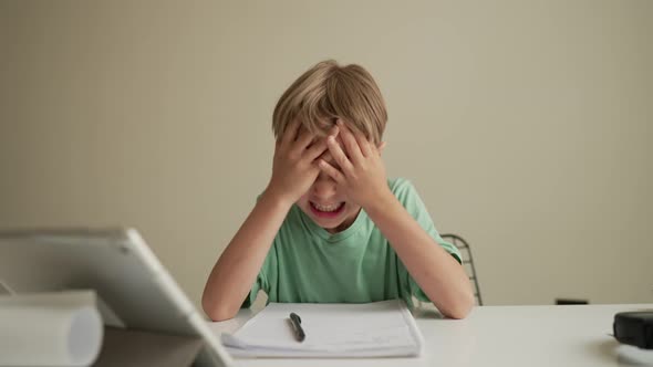 7 Yeas Old Boy Sitting at Table in Room and Crying While Working on Hard Homework alt