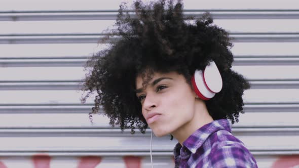 Portrait of pretty Afro American Female on street looking listening to music on headphones