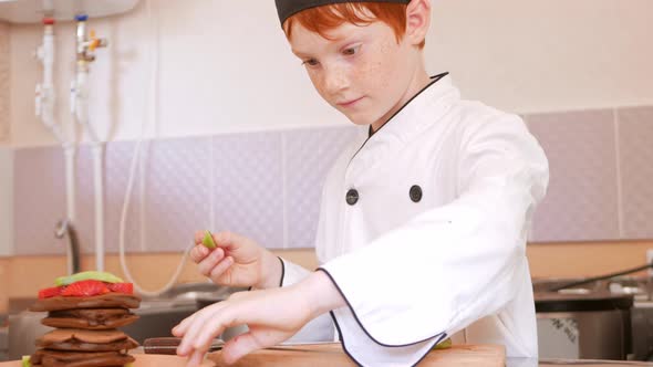 Child Boy in Chef's Costume Prepares Chocolate Pancakes in Kitchen in Cafe
