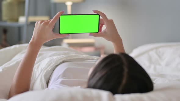 Latin Woman Watching Green Screen of Smartphone in Bed Chroma Screen alt