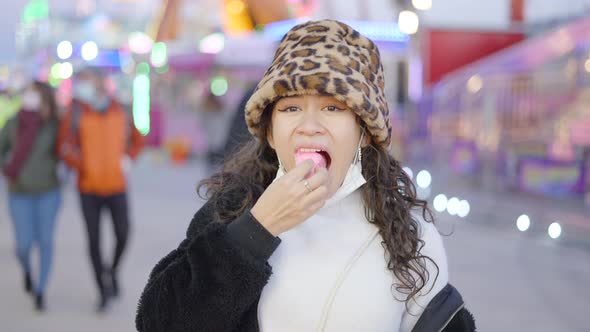 Cute Girl Smiling and Eating a Piece of Fluffy Candy Floss in a Fair and Showing a Big Thumb Gesture alt