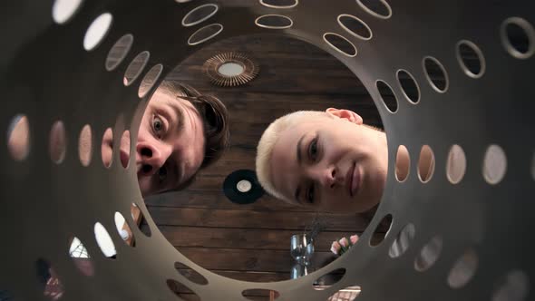 Man and Woman Look Inside Trash Can or Perforated Pipe Look at Each Other They are in Shock alt