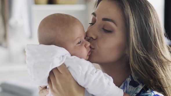 Delighted Young Mother Holds and Kisses Small Baby Closeup