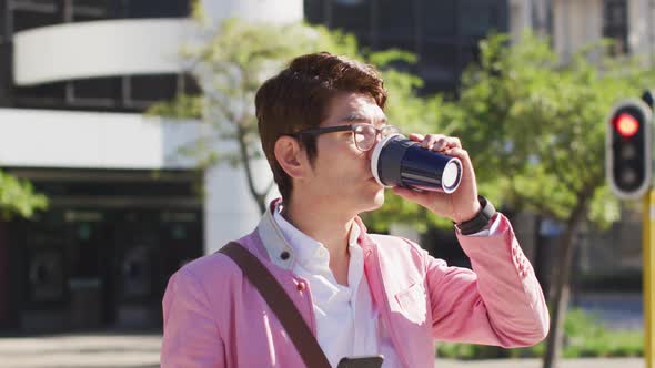 Asian man drinking coffee and using smartphone while crossing the street alt