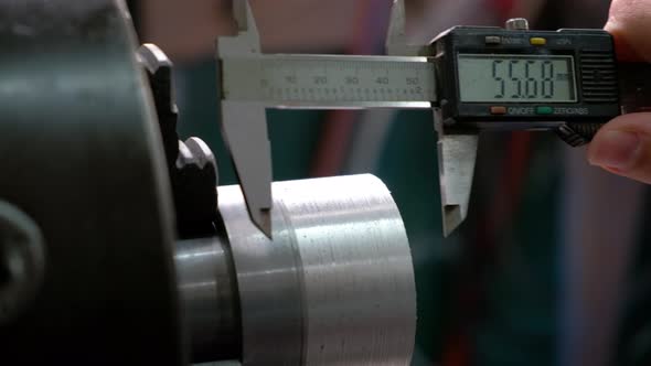 Worker measuring an aluminum metal piece on lathe with calliper alt
