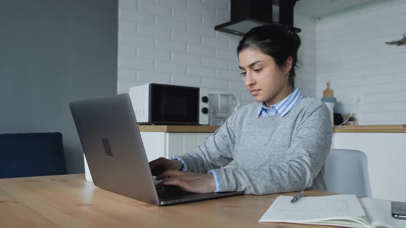 A Young Indian Woman Works At Home, Does Tasks On A Computer And Writes Notes In A Notebook alt
