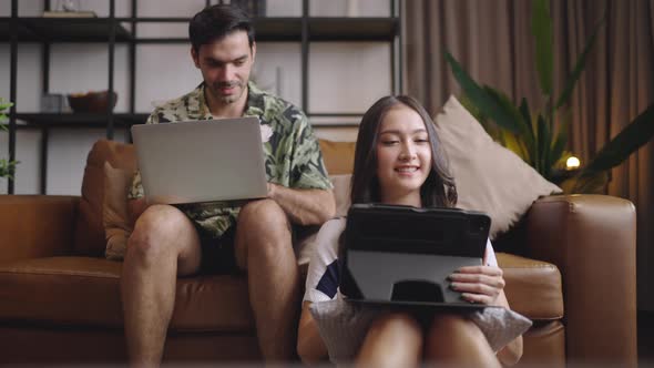 Young couple using tablet and laptop together on sofa in living room at home