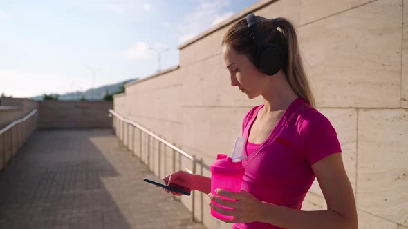 Young Woman is Resting After Morning Workout in Street Checking Message in Smartphone alt