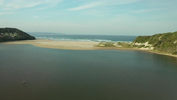 Aerial of river mouth streaming towards ocean waves on sandy beach alt