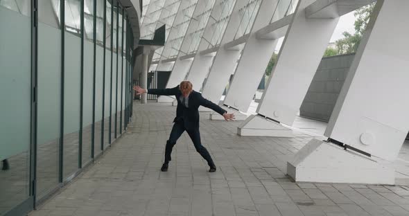 Happy Businessman in Wireless Headphones Listening to Music and Dancing Outside Near Office Building alt