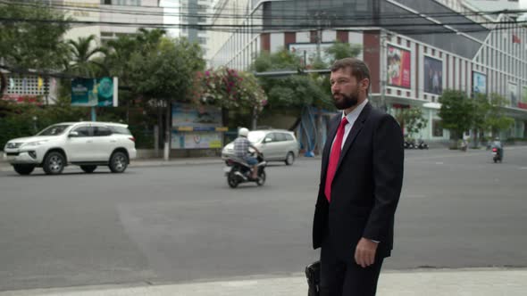 A Senior Businessman with a Beard in an Expensive Suit and Tie Walks with a Briefcase in His Hands alt