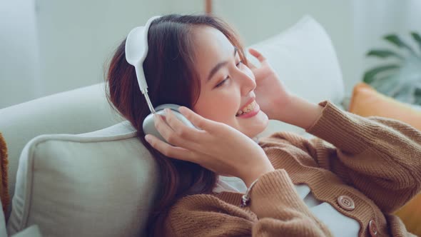 Serene asian woman relaxing on comfortable couch with wearing headphones in living room alt