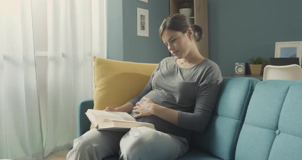 Pregnant woman reading a book and relaxing on the sofa