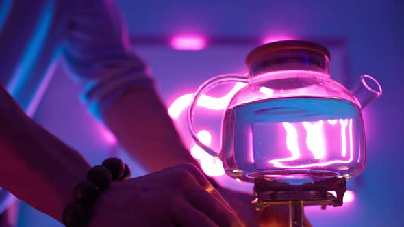 Man Turns on the Gas Burner To Boil Water To the Teapot Neon Lights Background alt